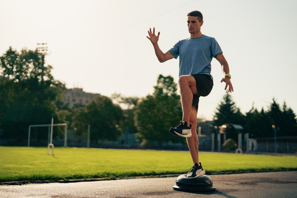 Young athlete doing a single-leg balance exercise on a Bosu ball at an outdoor track