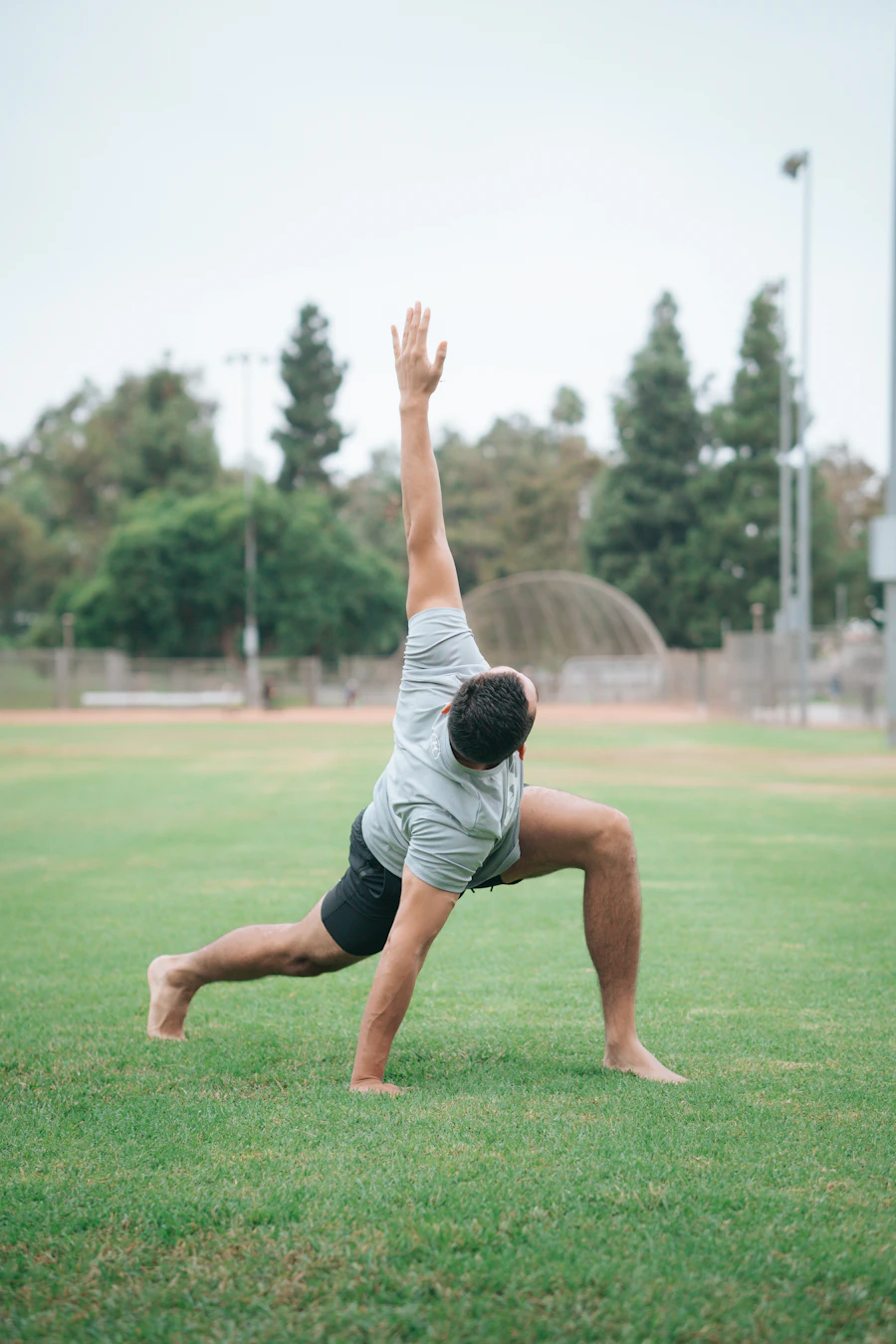 Athlete moving through a solo lunge-and-reach mobility stretch on a grass field
